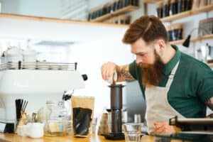 Replay Products | A bearded man pouring coffee in a coffee shop with eco-friendly packaging.