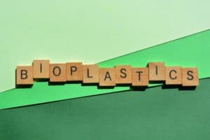 Replay Products | Bioplastics spelled out in wooden blocks on a green background, representing eco-friendly packaging.